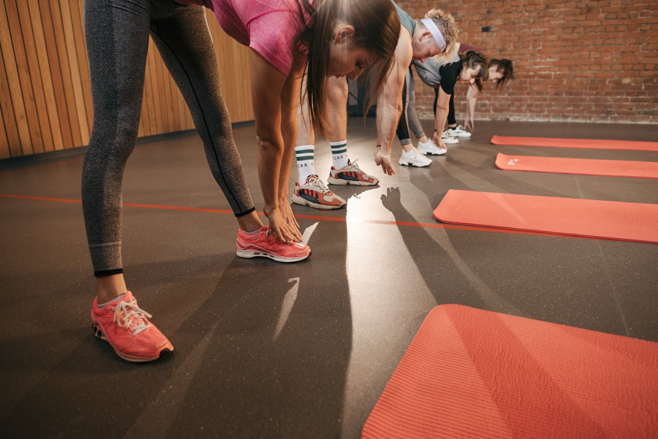 O Nas A diverse group stretches on red mats in a gym setting, enhancing fitness.