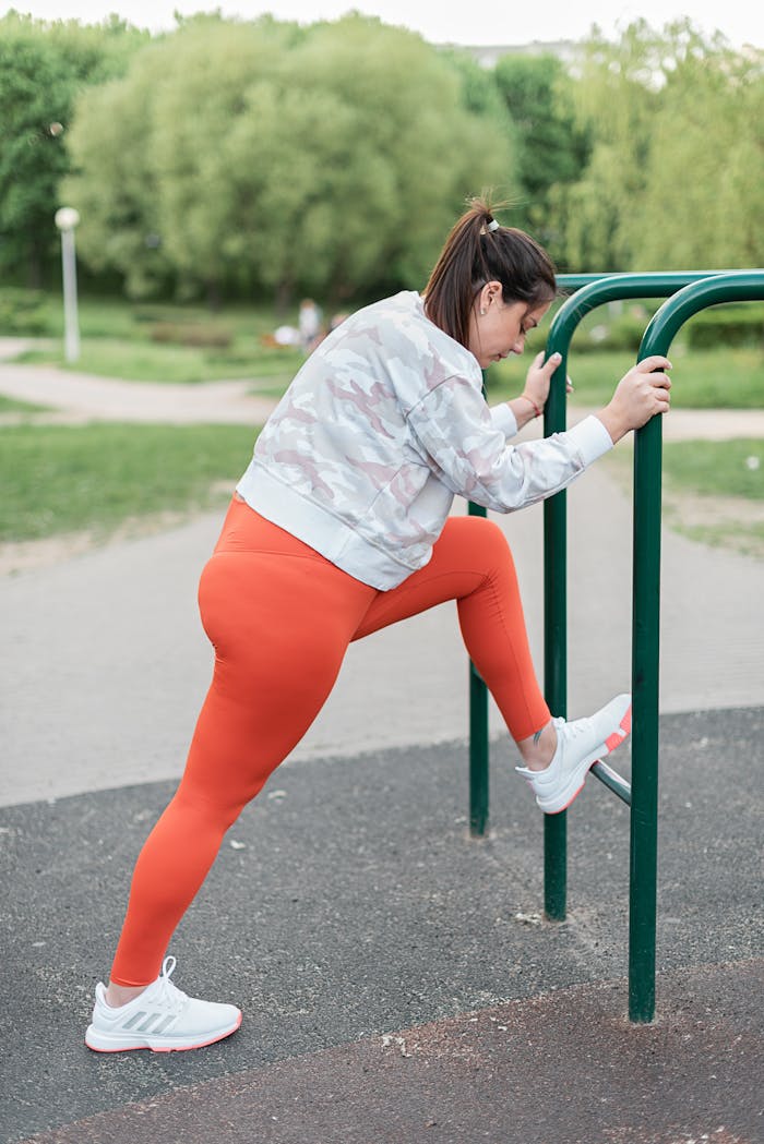 Trening personalny A woman exercises at an outdoor gym, stretching and preparing for a workout in vibrant sportswear.