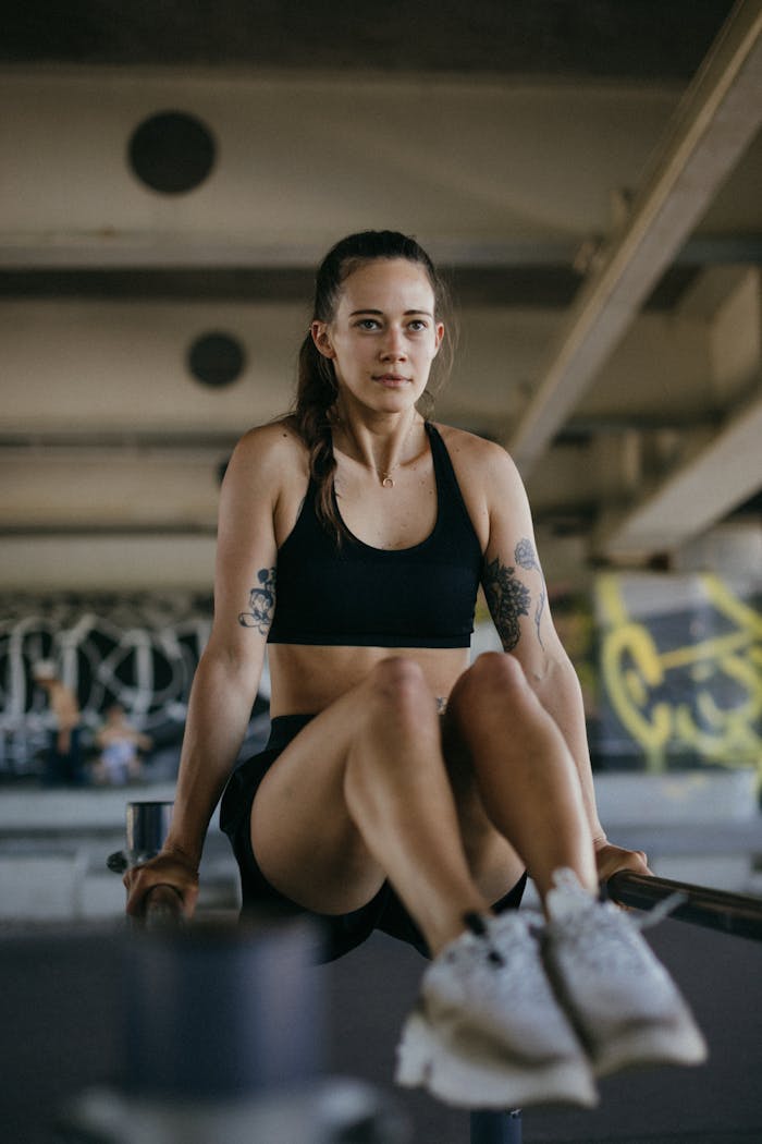 Trening personalny Young woman focuses on strength training on parallel bars in an urban gym setting.